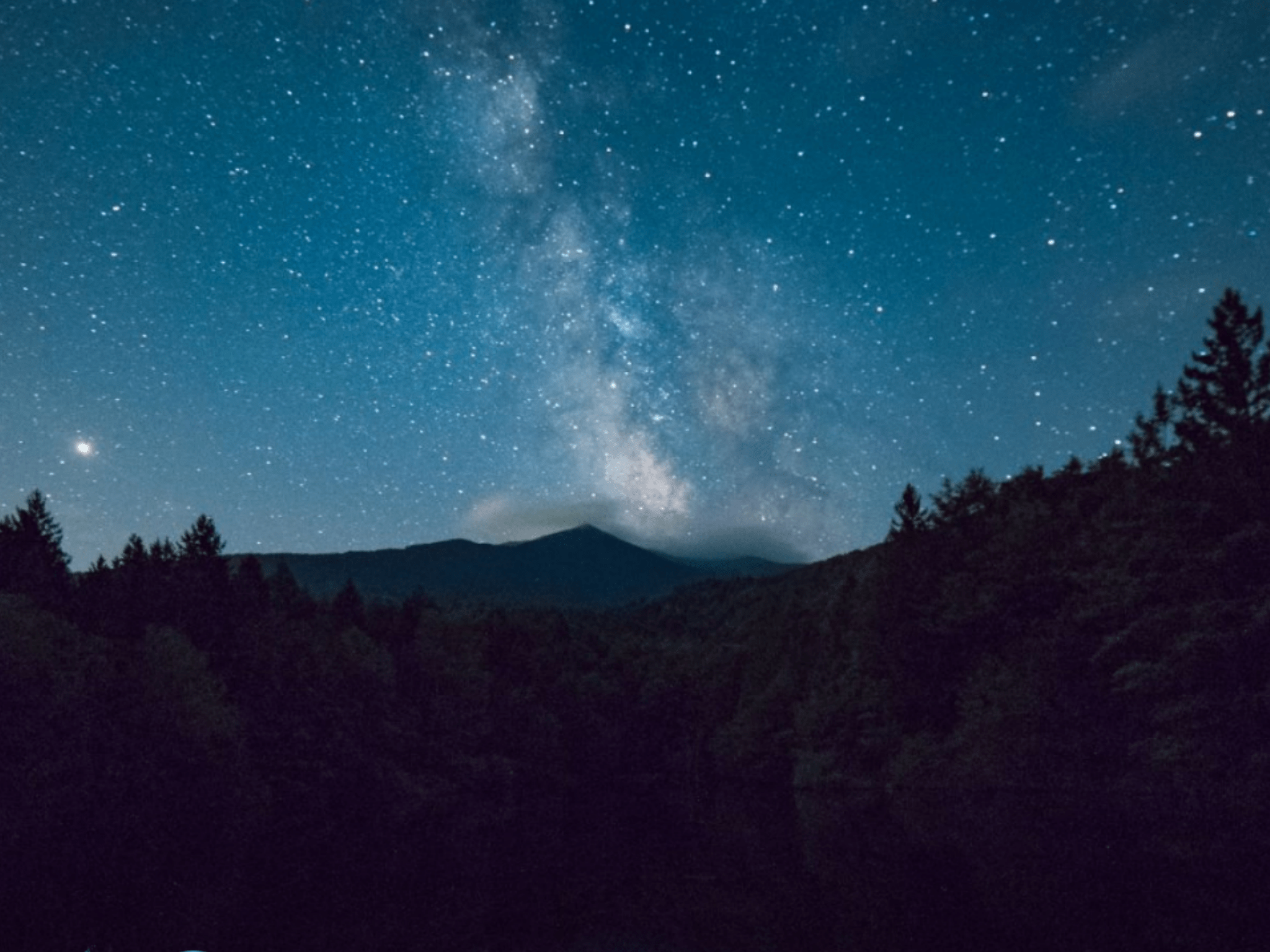 Landschaft mit Bergen und Wald und Sternenhimmel bei Dämmerung.