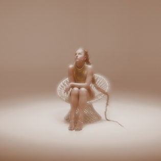 Cover von Amilli – “Hazy Days”; Foto des Artists in einem weißen Raum auf einem weißen Stuhl