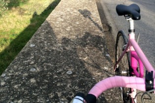 Rosa Rennrad steht am Straßenrand neben einem Grünstreifen.