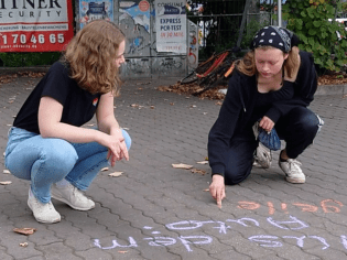 Kristina und Mia schreiben mit Kreide erfahrene sexistische Sprüche auf den Boden