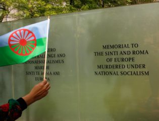 Hand mit Flagge vor Gedenktafel