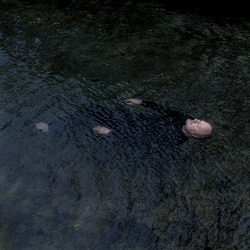 NEW NATIVE – Until It All Stops Spinning; Foto eines weißen Mannes, der in schwarzem Wasser treibt