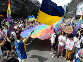 Demonstrierende halten Regenbogenfahren und einePerson schwenkt Fahne der Ukraine