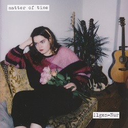 ILGEN NUR – Matter of Time; Fot einer weißen Frau mit Rosen im Schoß auf einem Vintage-Sessel, im Hintergrund stehen zwei Gitarren