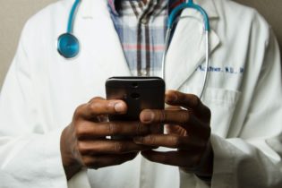 Arzt in weißem Kittel hält ein Smartphone in seinen Händen.
