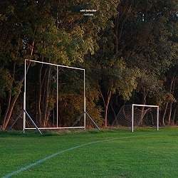 Albumcover von ODD BEHOLDER - Lighting (Feijká Remix); ein Foto von einer Wiese, dem Gerüst einer Plakatwand und weiter hinten ein Fußballtor ohne Netz; dahinter ein Wald