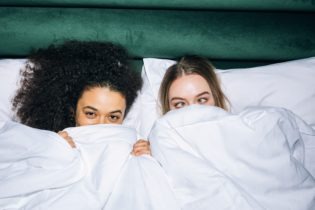 [Two Young Girls Lying on White Bed]