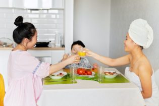 Foto von zwei asiatisch-stämmigen Frauen, die mit einem Kind am Frühstückstisch sitzen